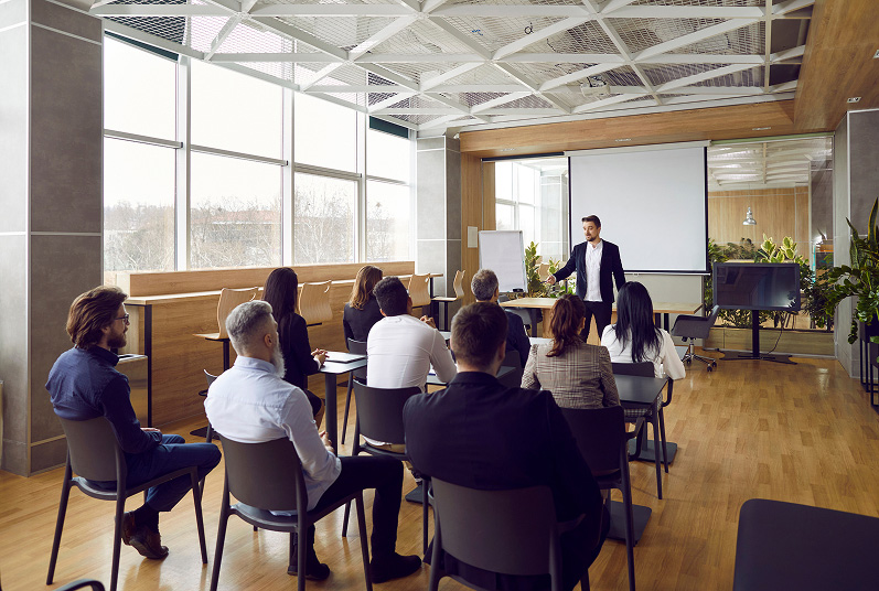Face-to-face training session with an instructor presenting to a group of professionals in a modern classroom environment.